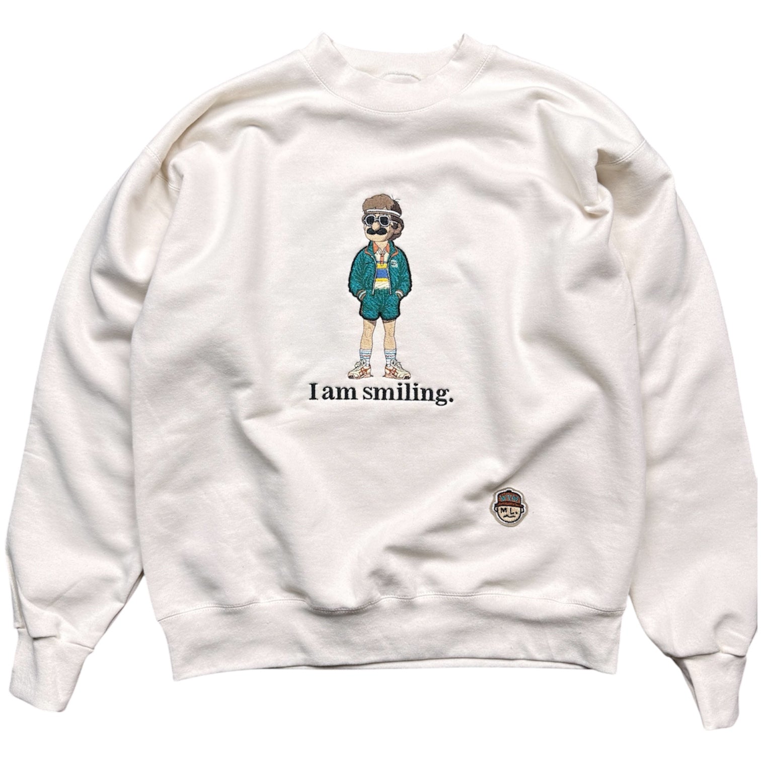 Oatmeal colored sweatshirt with cartoon character and 'I am smiling.' text on a white background