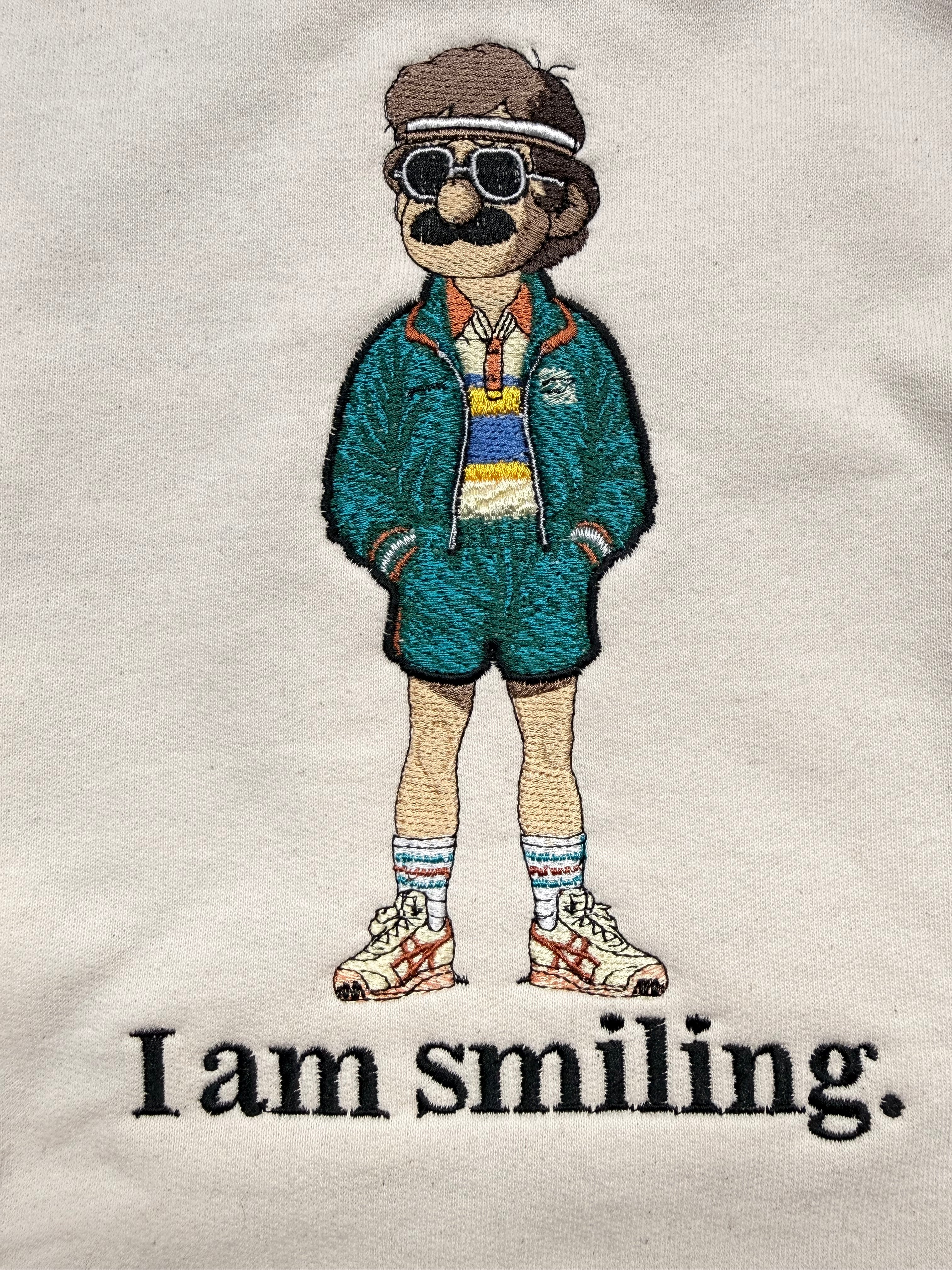 Embroidered design of a person wearing a green jacket with text 'I am smiling.' on a white background.