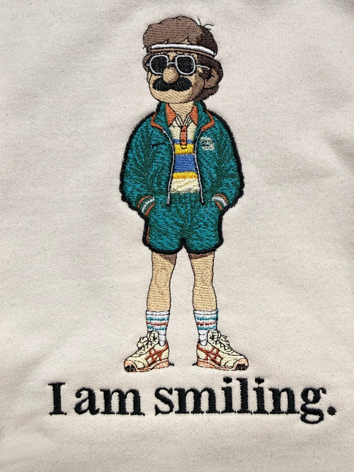 Embroidered design of a person wearing a green jacket with text 'I am smiling.' on a white background.