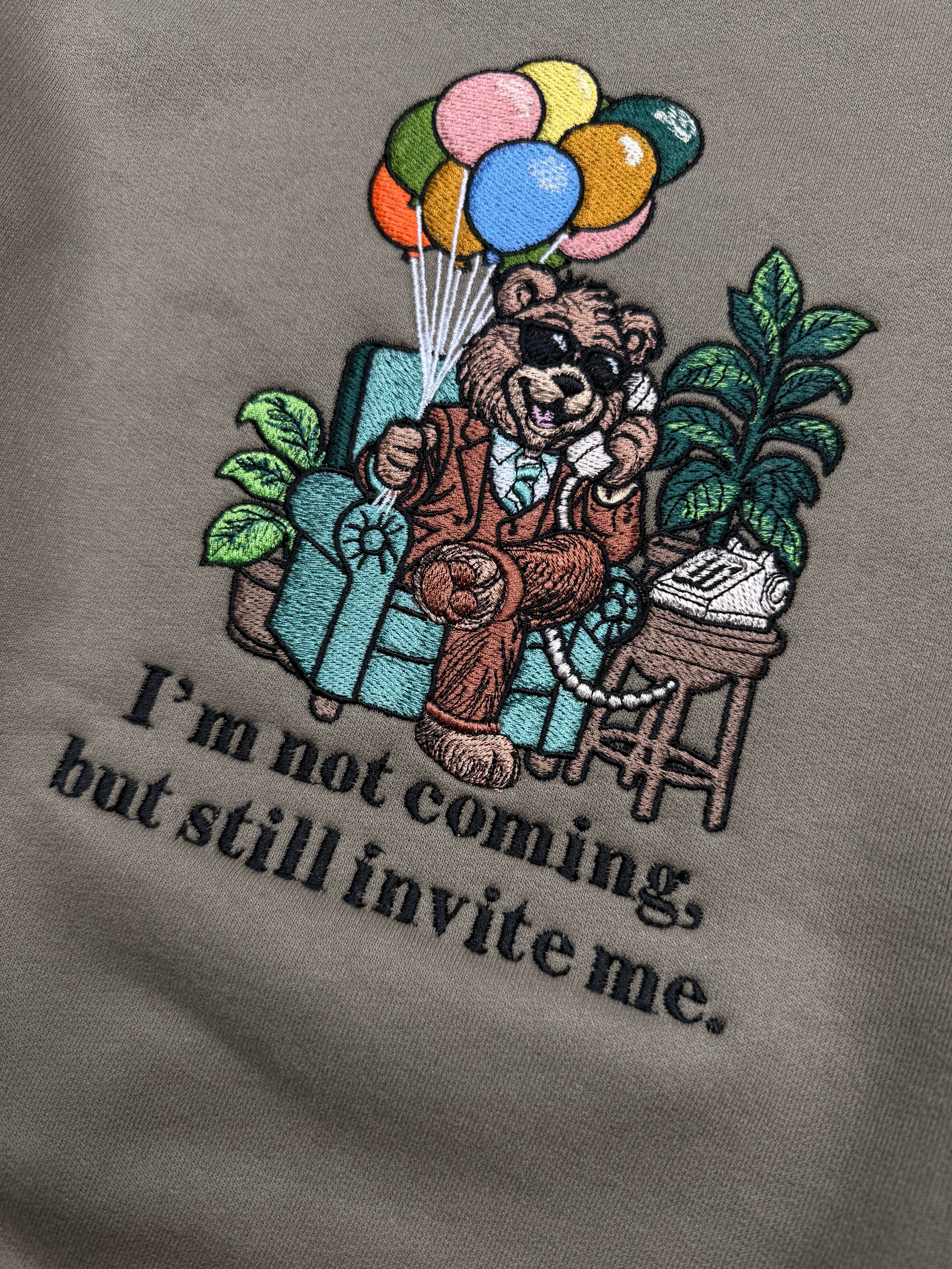 Embroidered design of a teddy bear with balloons and flowers on a white background.