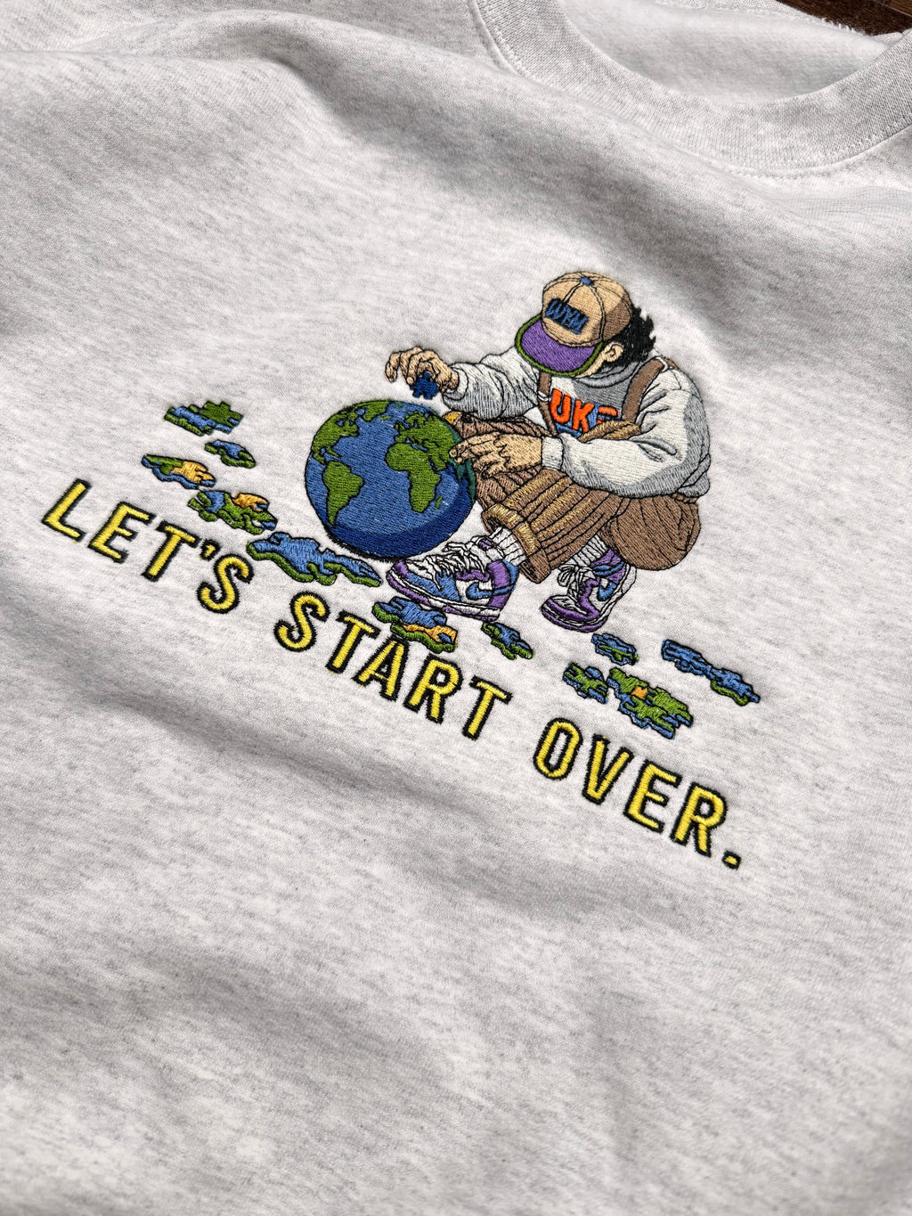 Gray sweatshirt with a graphic of a person holding a globe and text 'LET'S START OVER.'